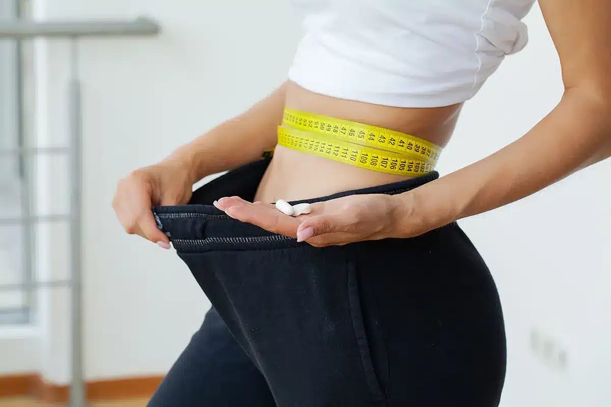 Woman holding weight loss pills and loose pants.