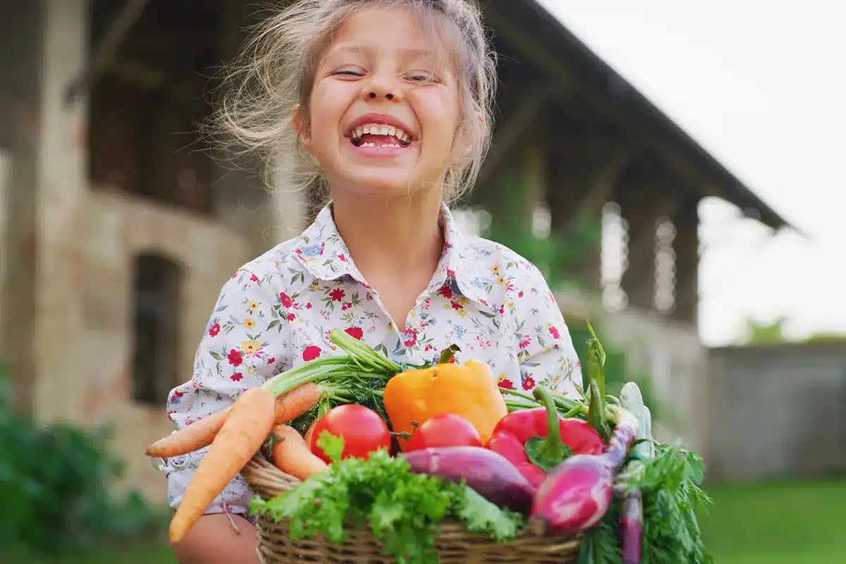 Child holding a basket of vegetables.
