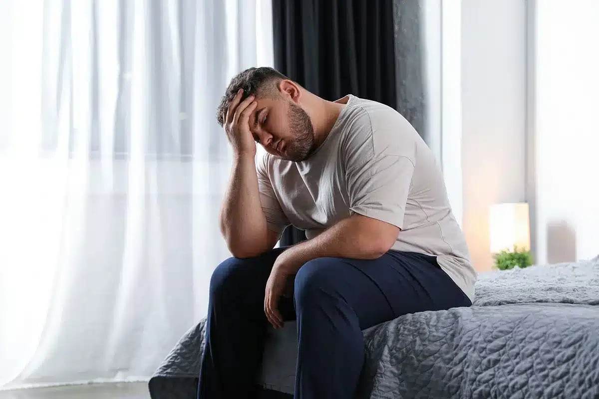 Upset overweight man sitting on bed.