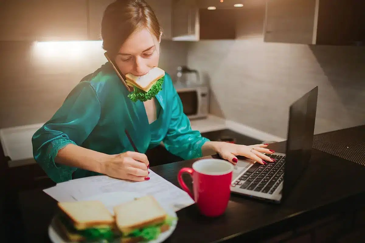 Busy woman working from home, eating lunch.