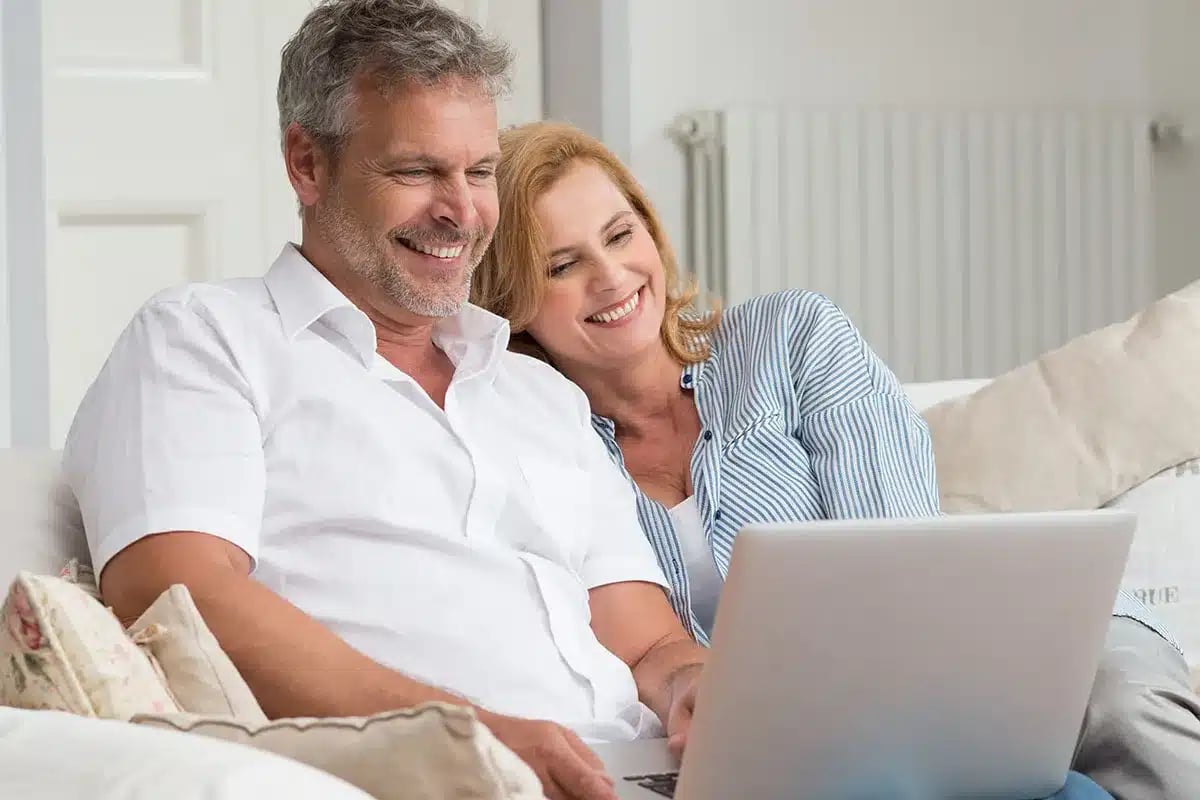 Happy couple using laptop on couch.