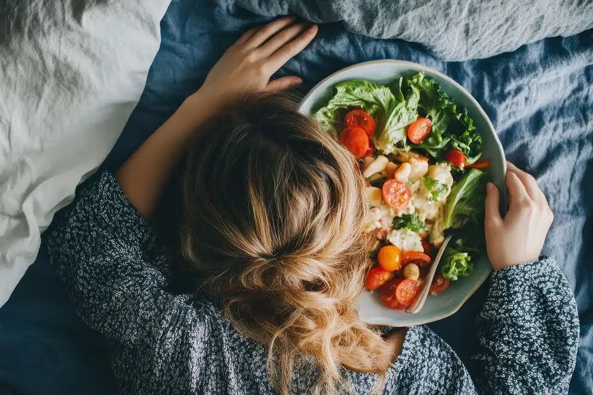 Woman eating healthy salad in bed.