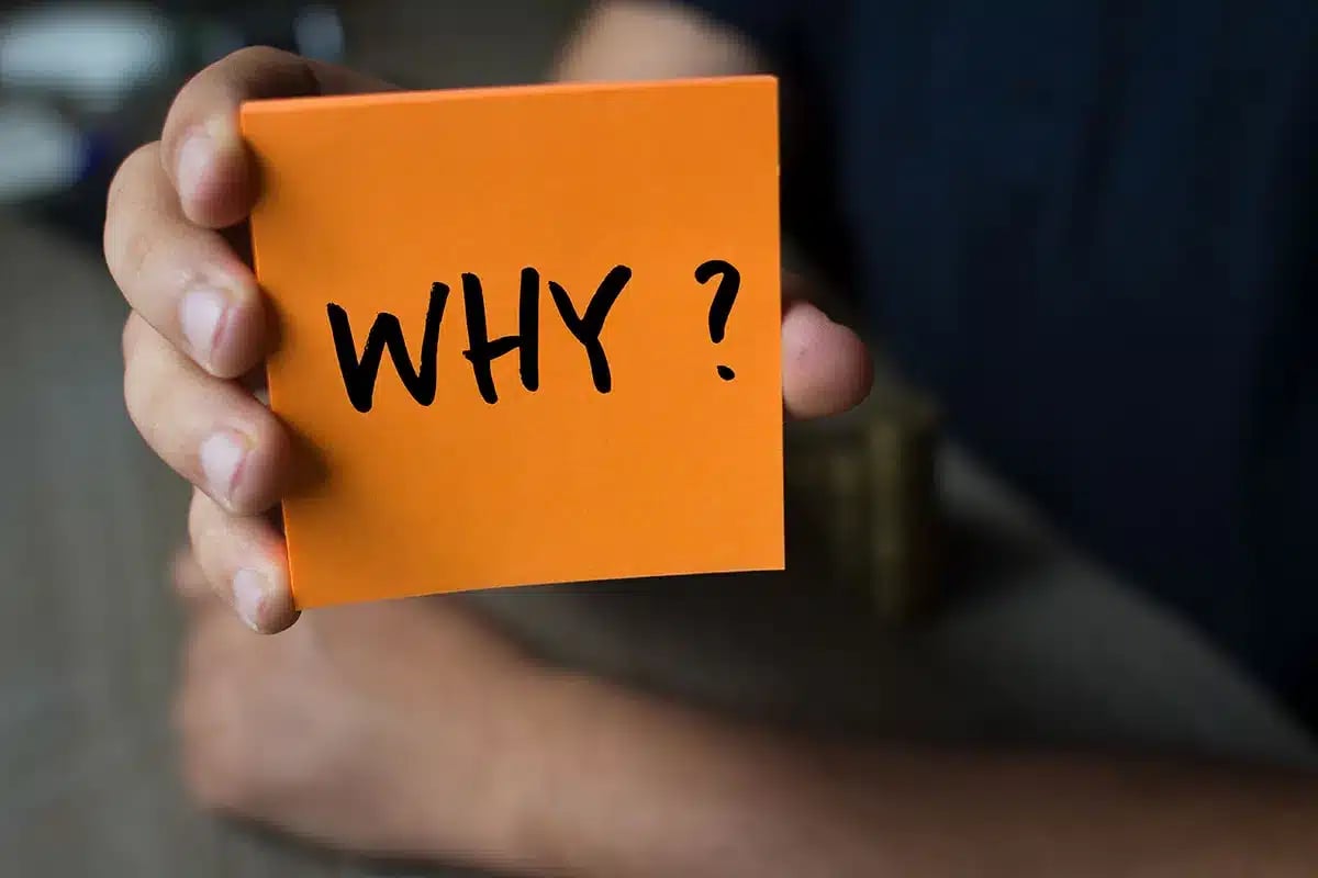Hand holding a note that says "Why?"