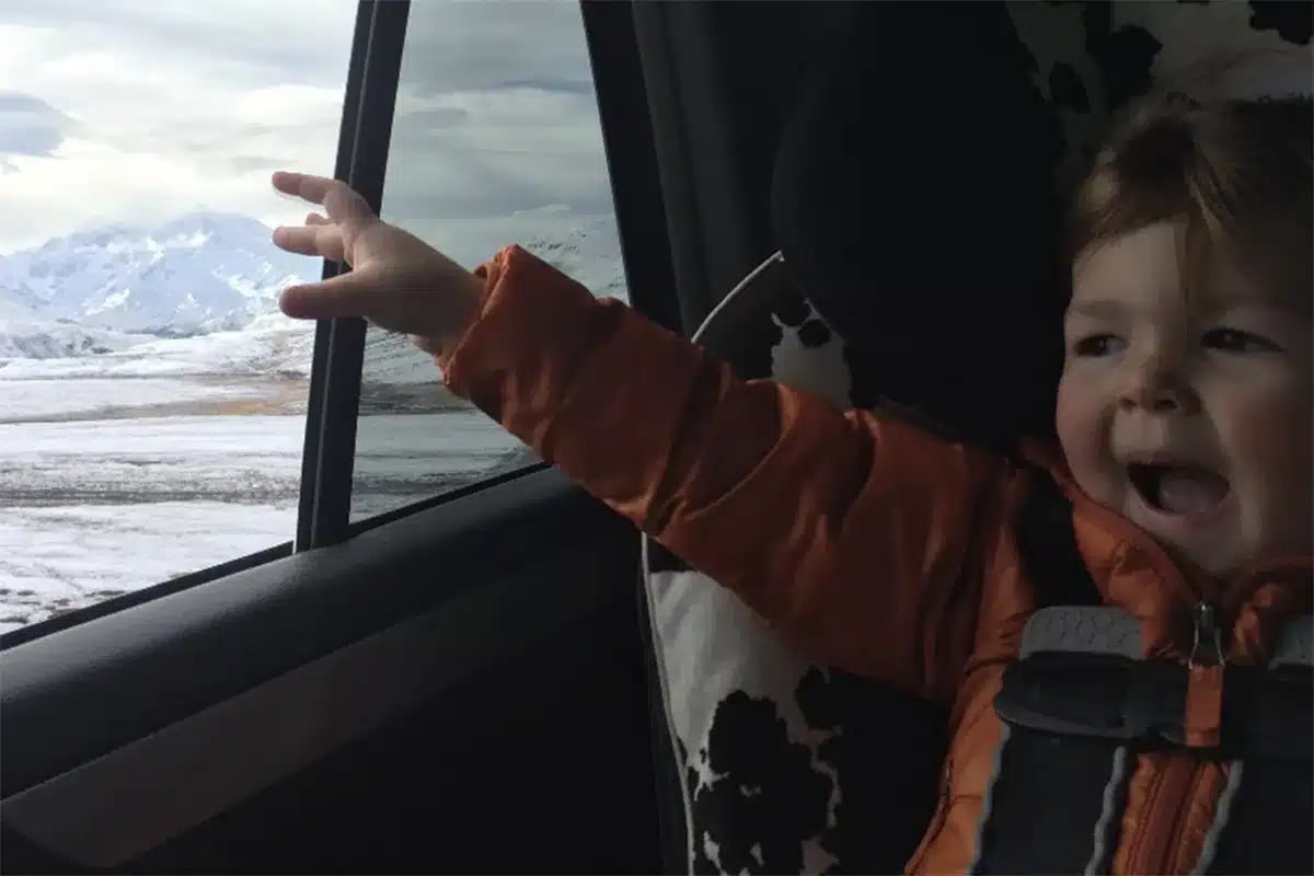 Baby reaching for snowy mountain view.