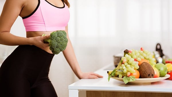 woman holds a large head of broccoli in front of a kitchen counter